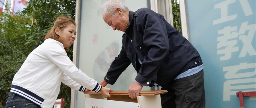 10月9日，在南昌市青山湖區順外路口的公交站臺旁，李樹子（右）和社區工作人員把剛修好的長板凳擺放到公交車站。